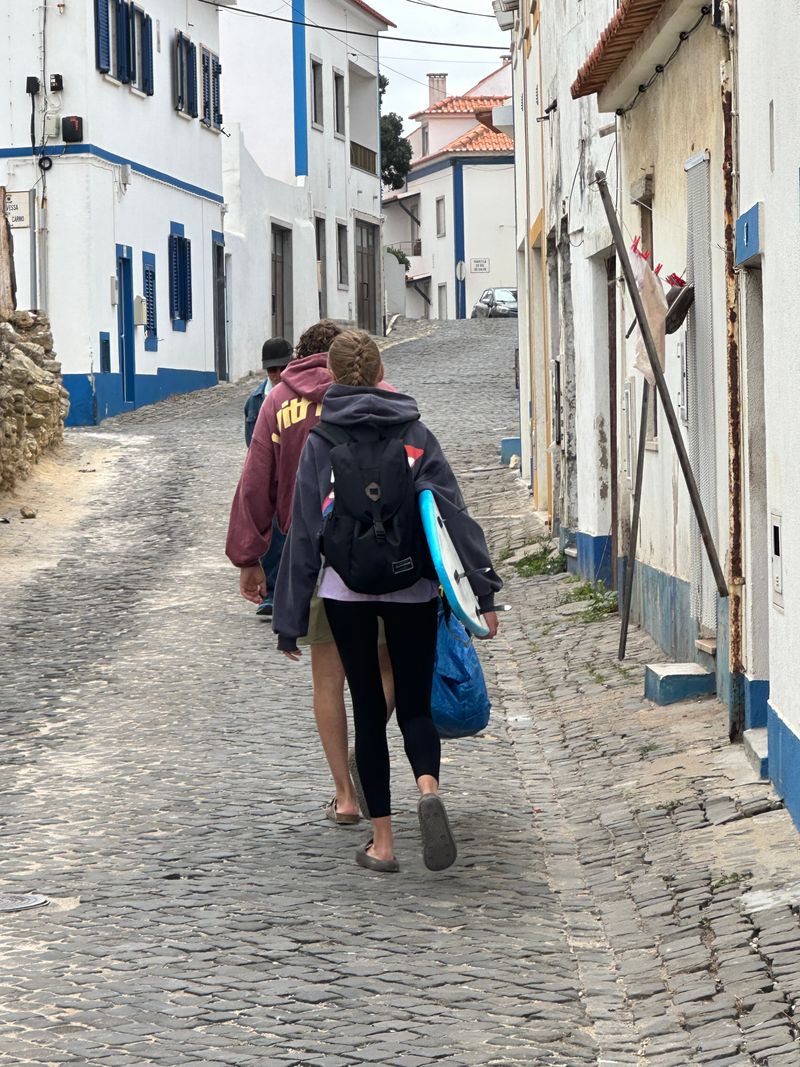 Surfers carrying boards through a cobblestone street in Ericeira, Portugal