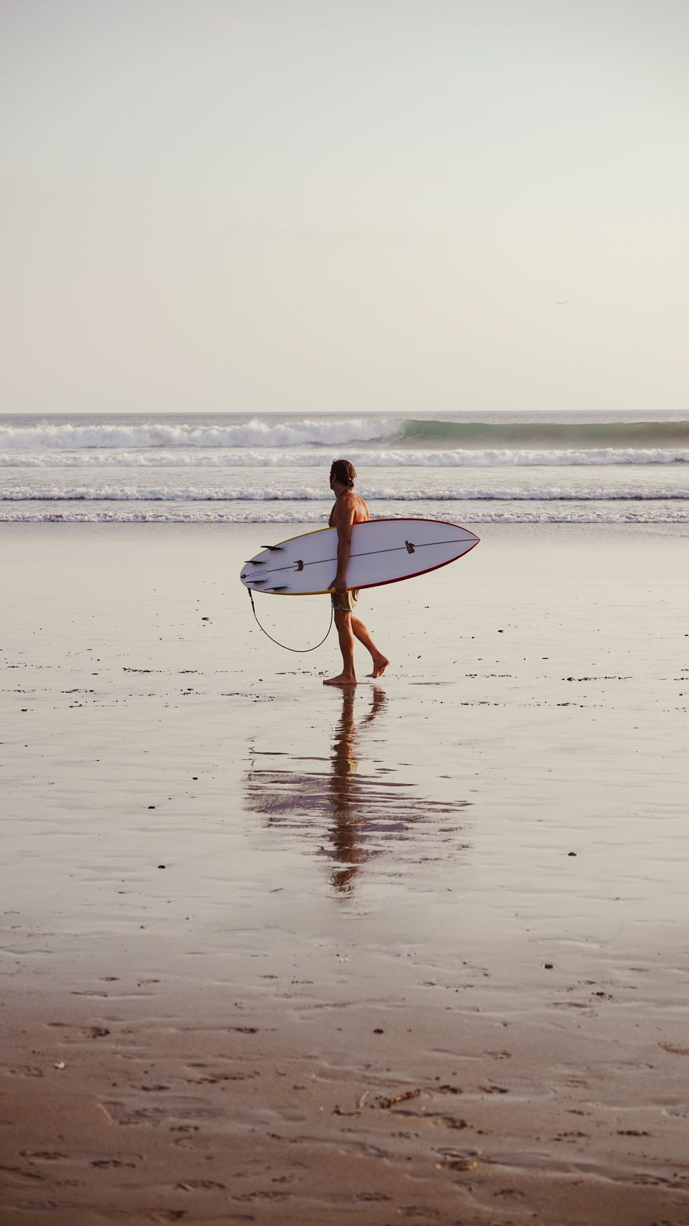 Surfer carrying a board along a quiet tropical beach near Nosara, Costa Rica