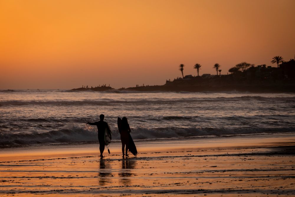 Surfers walking the beach at sunset in Taghazout, Morocco