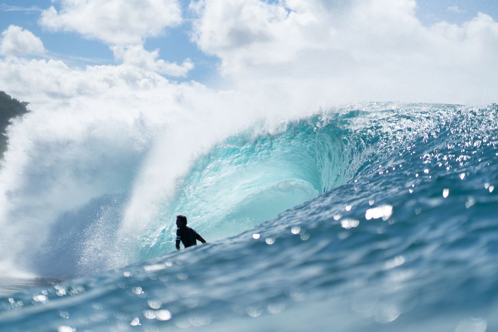 A surfer silhouetted at the base of a massive, heavy barreling wave